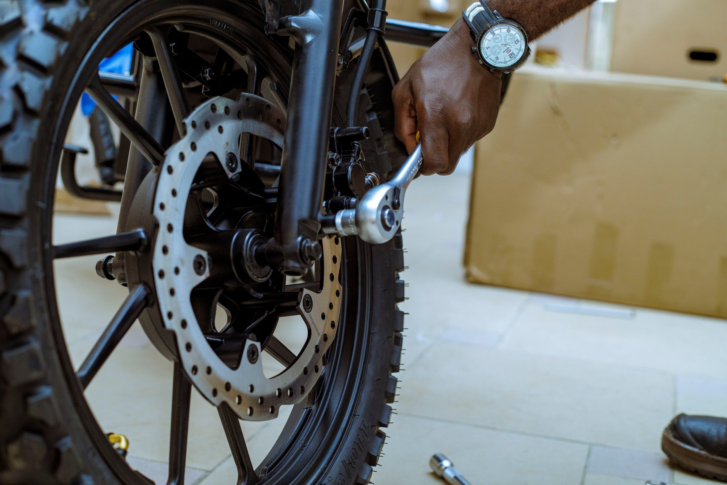 Un technicien Ehu serre l'étrier de frein avant d'une moto, clé à cliquet en main.