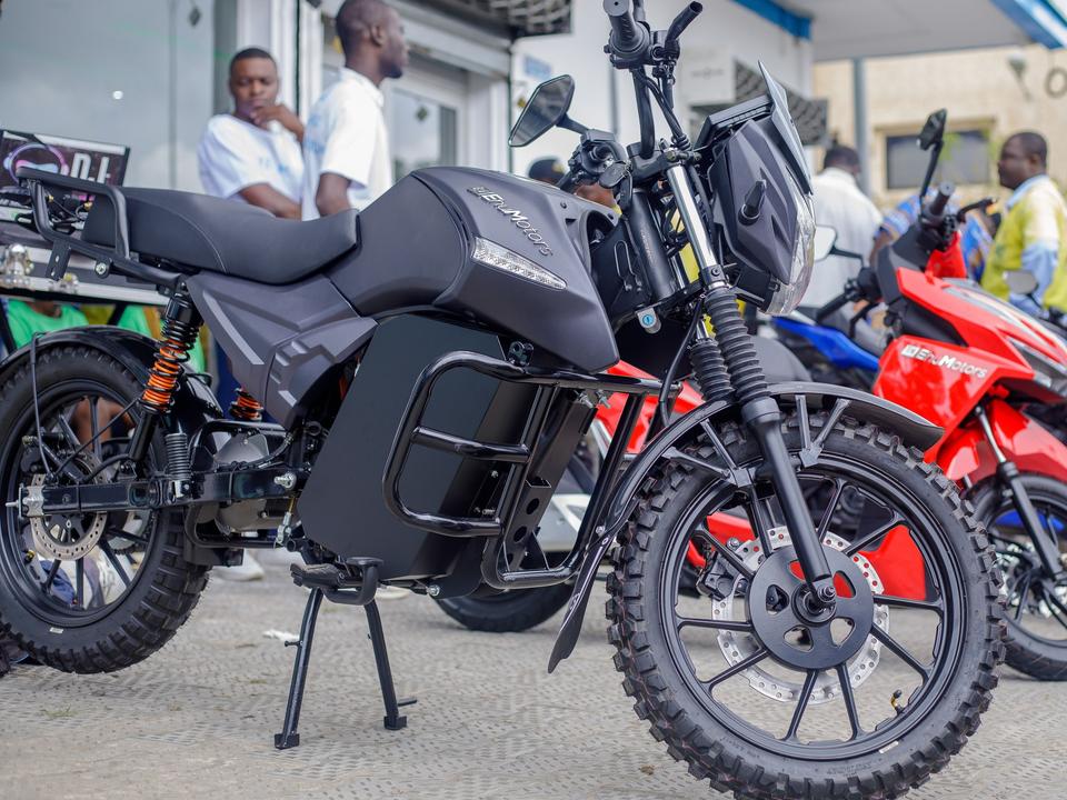 Une Finesse, moto électrique Ehu noire, garée devant le showroom de Cotonou, des conducteurs en gilet jaune derrière.